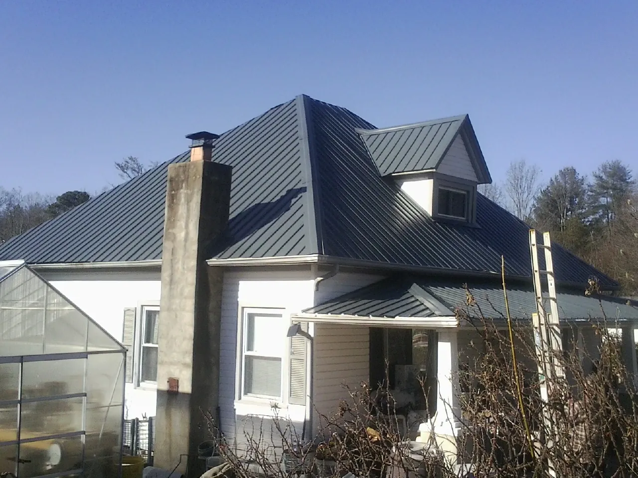 Dark blue standing seam metal roof on a white farmhouse with dormer — Slate & Tile Roof Repair by Roofing Brothers in Houlka