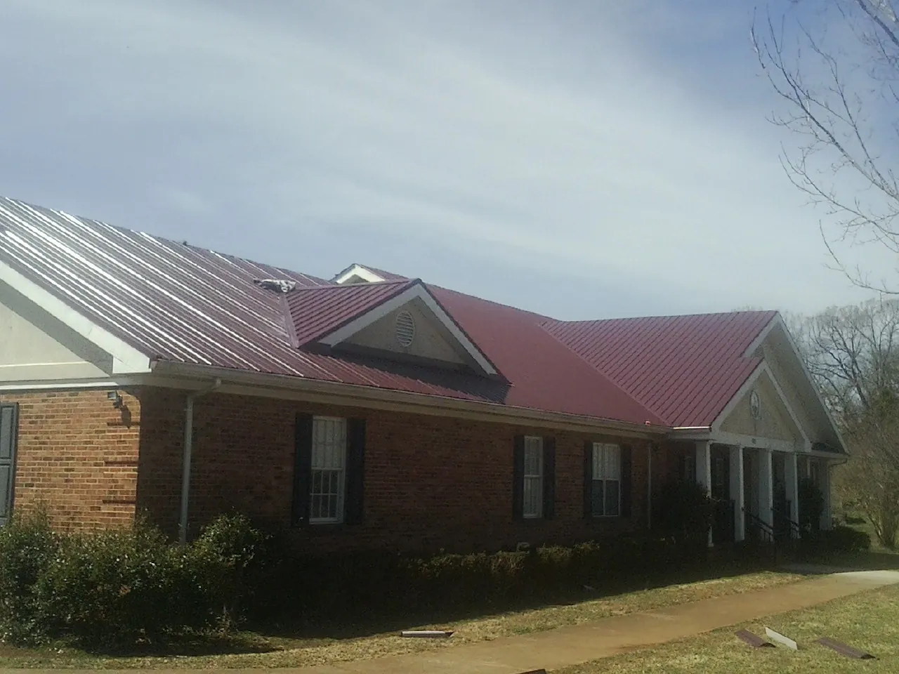 Red metal roof with gabled entries on a long brick building, from a Hail Damage Roof Repair job in Houlka