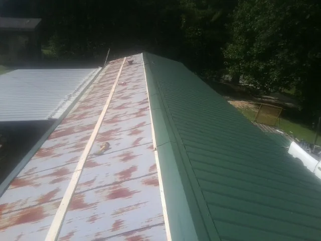 Old rusted panels beside newly installed green metal roofing — Wind Damage Roof Repair by Roofing Brothers in Houlka