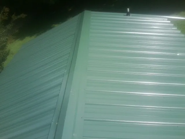 New green metal panels meeting at the ridge of a roof — Flat Roof Repair work by our crew in Houlka