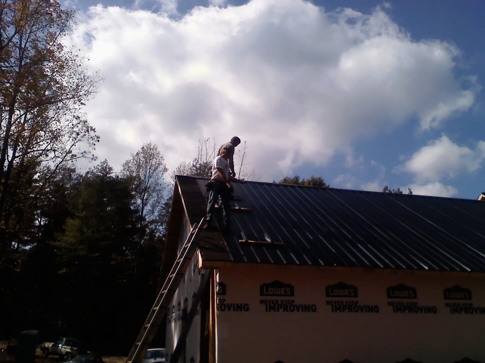 Roofer fastening dark metal panels high against a cloudy sky, from a Roof Inspection job in Houlka