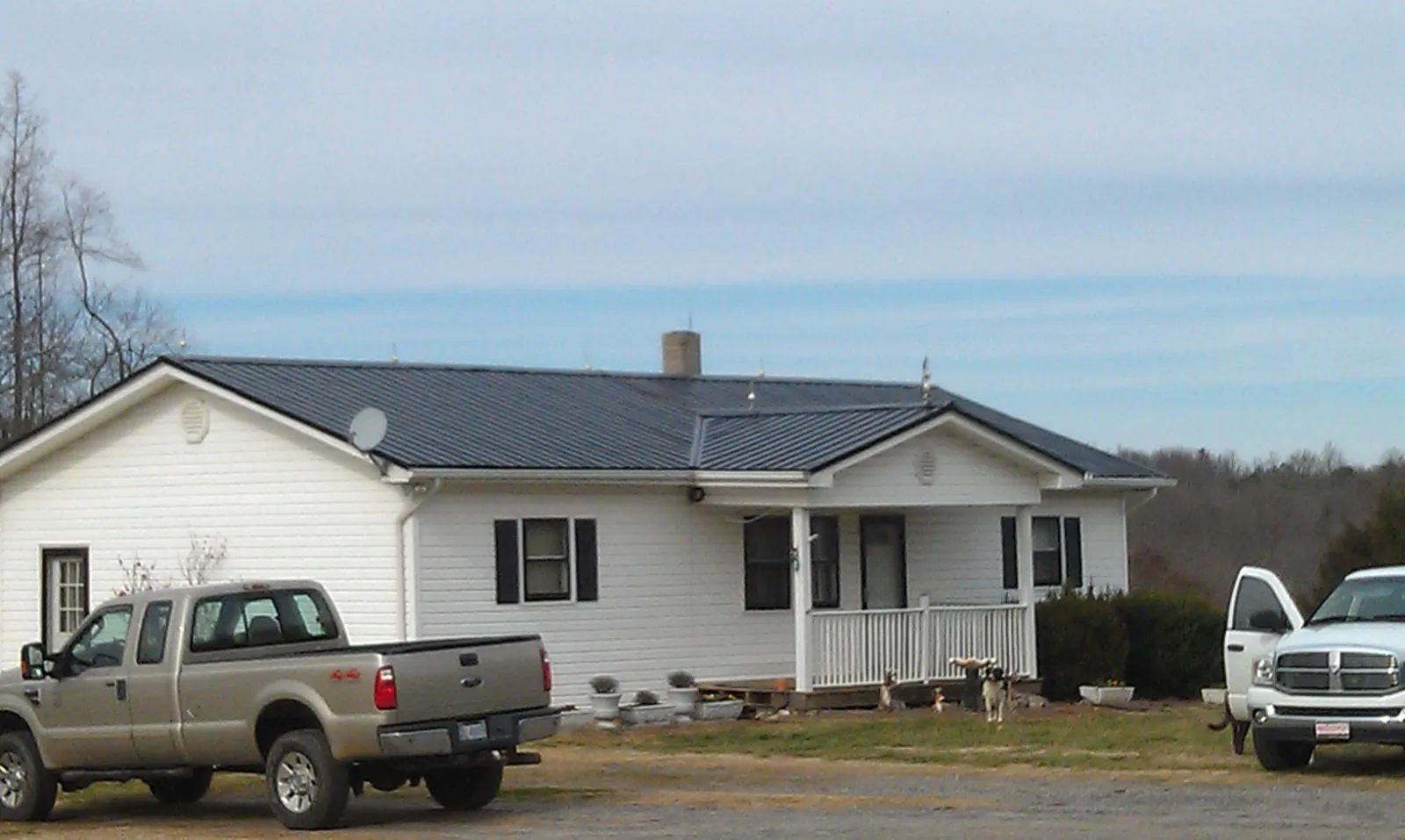 Finished dark metal roof on a white ranch home with work trucks parked in Houlka