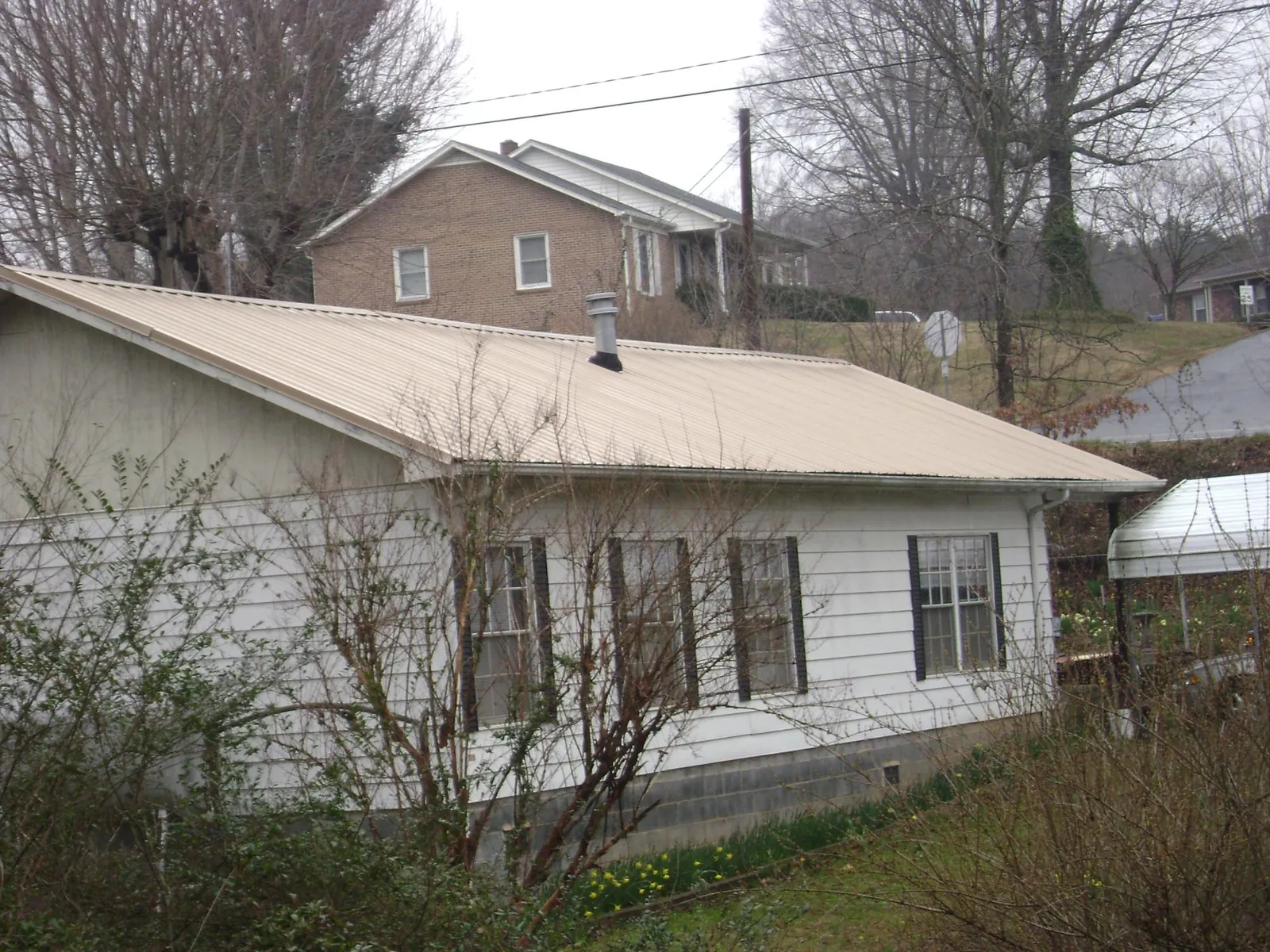 Tan metal roof on a white sided house set into a hillside — Commercial Roofing by Roofing Brothers in Houlka