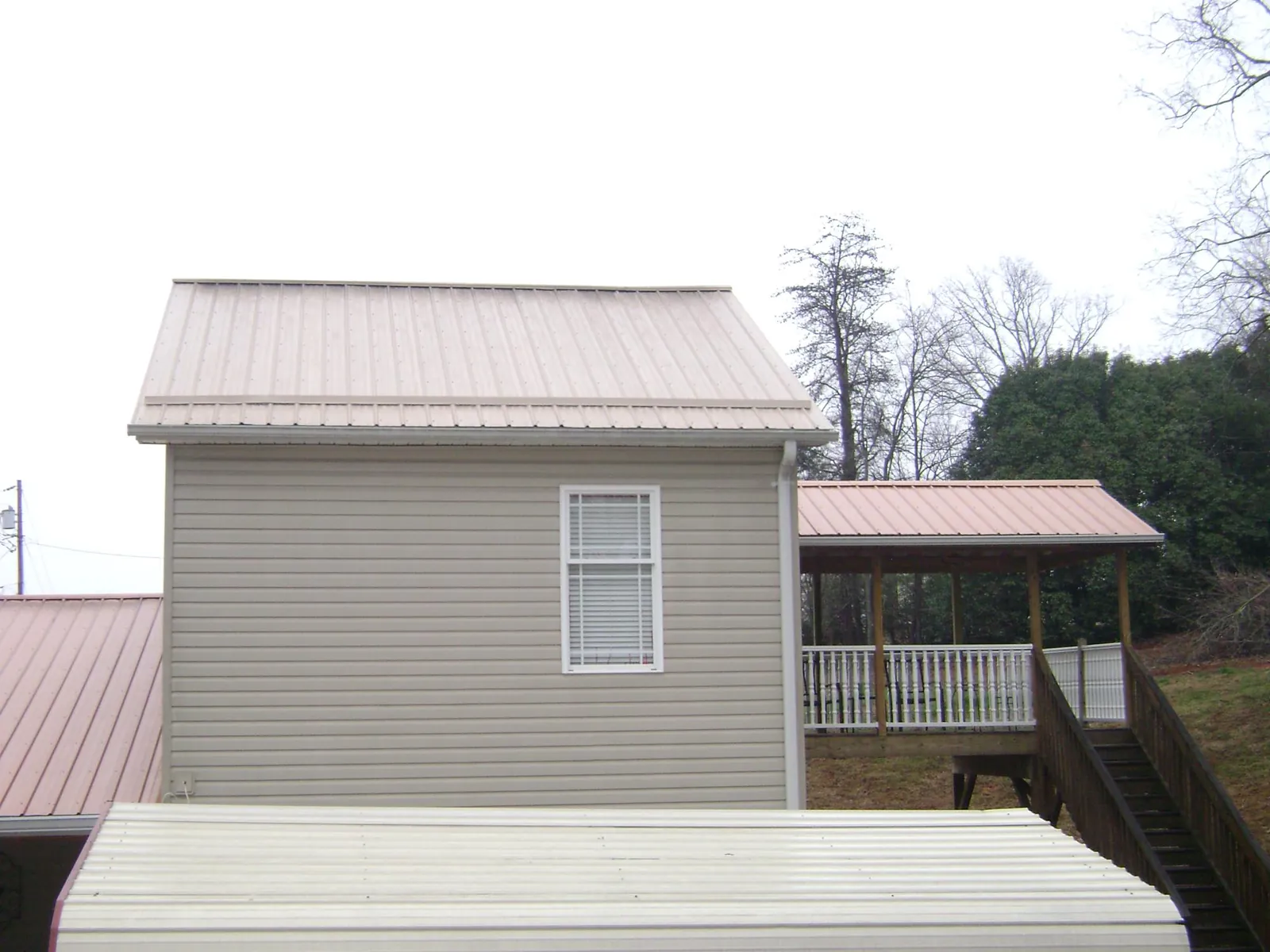 Tan metal roofs on a two story addition and attached porch, from a Roof Replacement job in Houlka