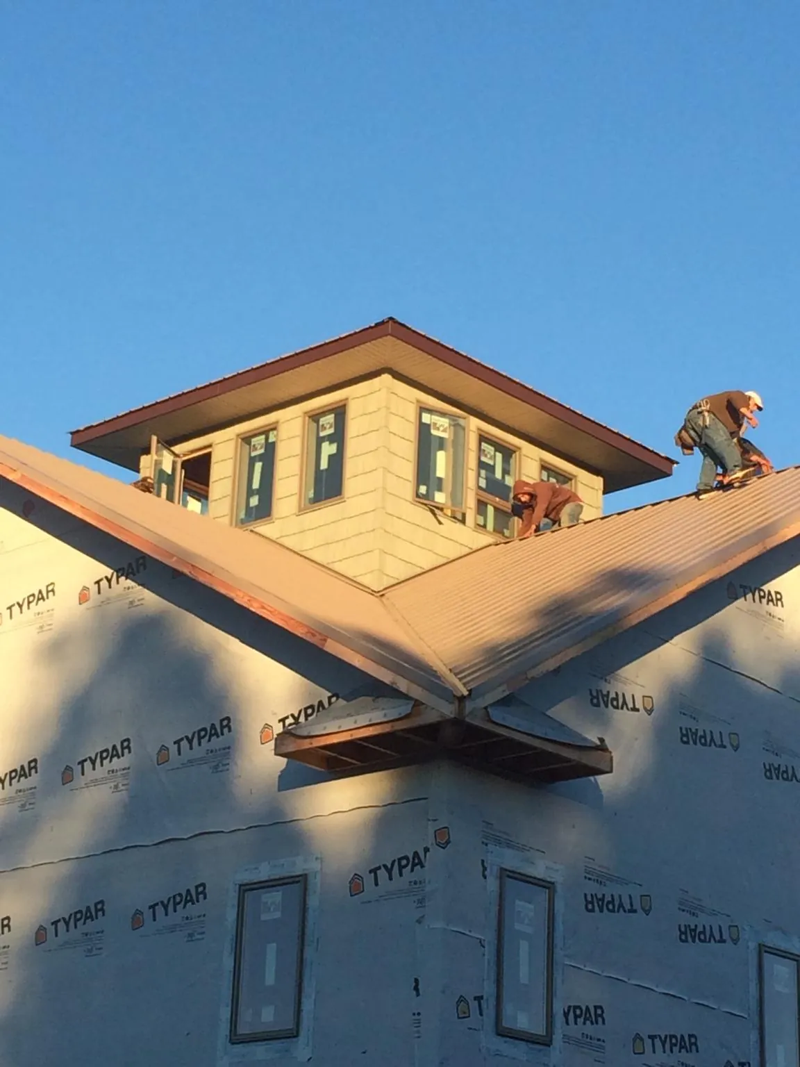 Roofers working around a rooftop cupola on a new metal roof at sunset — Roof Waterproofing in Houlka by Roofing Brothers